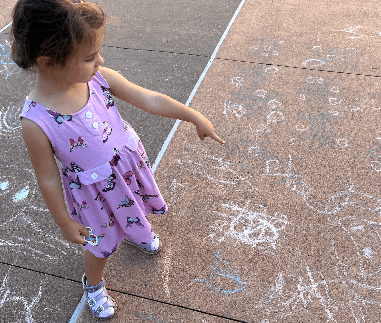 A girl in purple dress pointing at chalk art