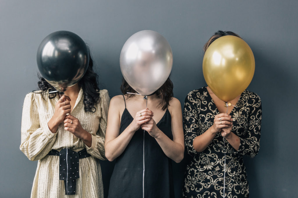 3 Women dressed up pretty holding balloons in front of their faces