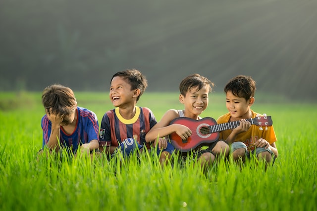 4 boys in a high grass field playing a guitar