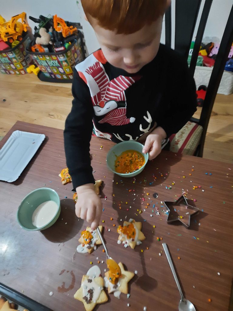 A little boy with orange hair decorating the star-shaped Christmas butter cookies with sprinkles and royal icing