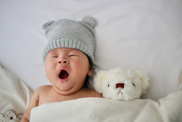 A baby yawning, a plush teddy bear next to it